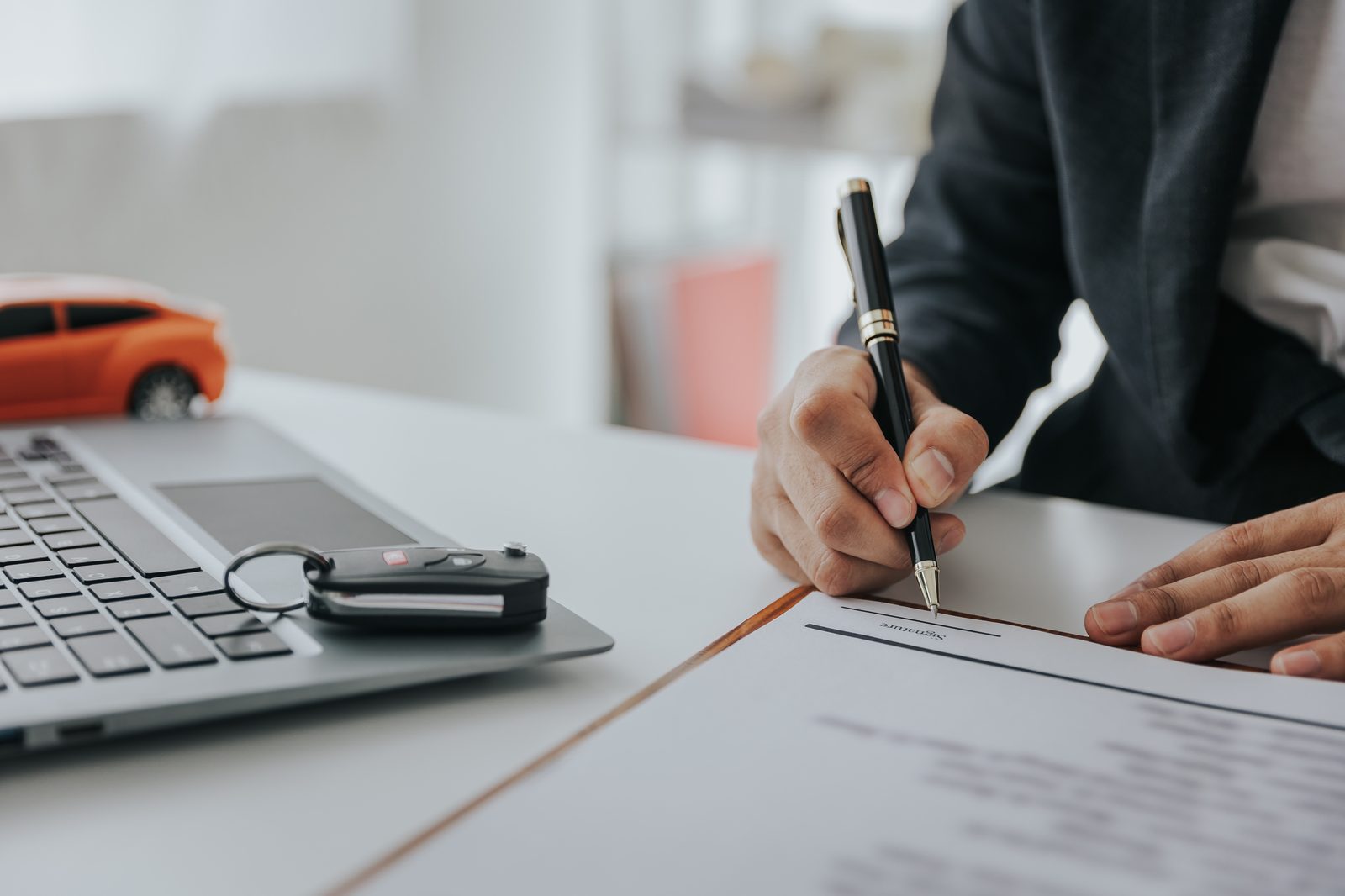 Cliente firma il contratto di vendita di un'auto usata con chiavi e laptop